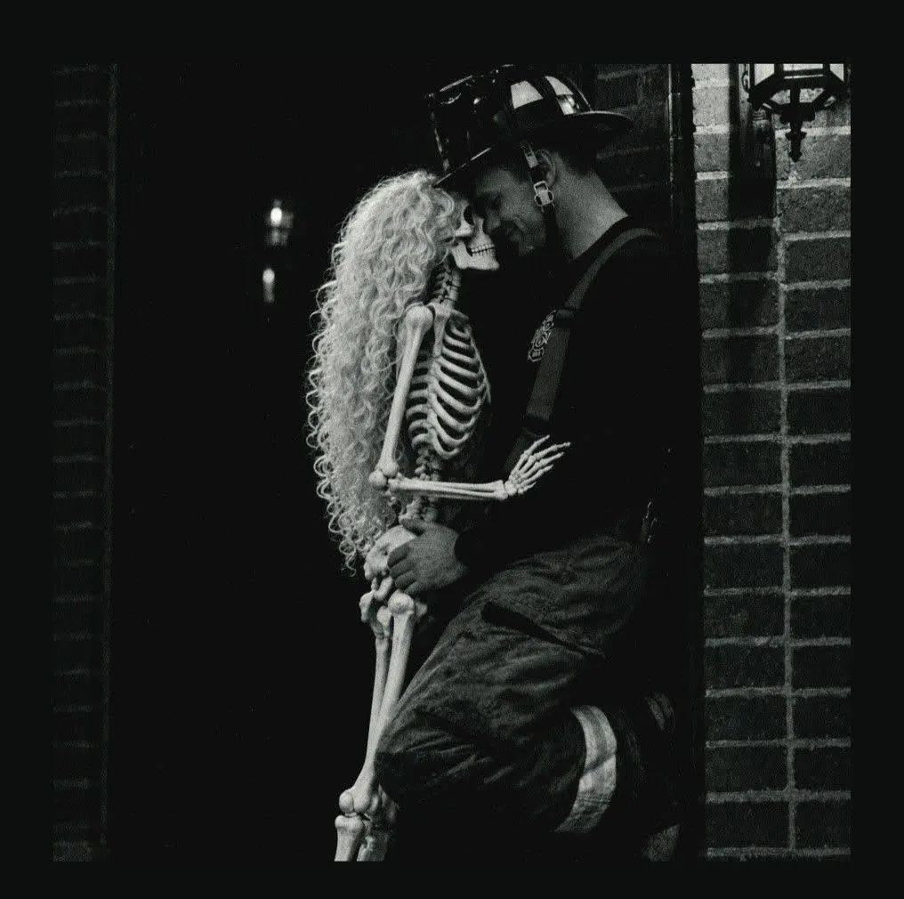 Chris in firefighter turnout gear, leaning in next to his skeleton girlfriend in a doorway
